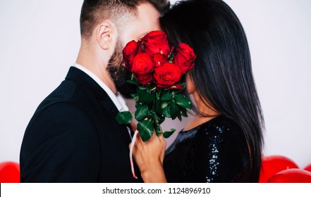 Beautiful Young Elegant Couple Are Kissing Behind Bouquet Of Red Roses. Happy Family. Love Concept And Holidays. Gift From A Loved One.