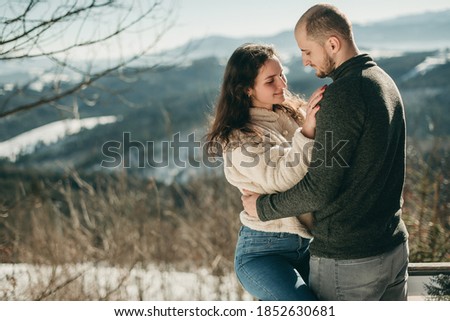 Beautiful young European couple in a sweater in the winter in the snowy mountains hugging and kissing. Man and woman, travel, nature. In love, girlfriend. Christmas holiday, vacation.