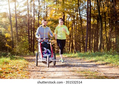 Beautiful Young Family With Baby In Jogging Stroller Running Outside In Autumn Nature