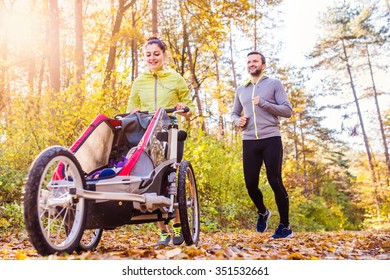 Beautiful Young Family With Baby In Jogging Stroller Running Outside In Autumn Nature