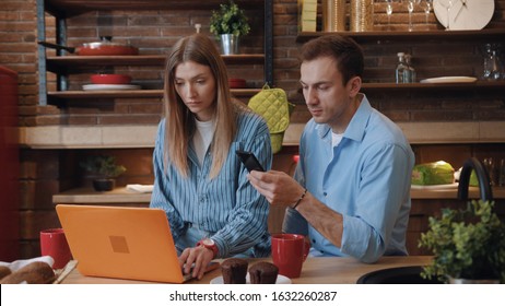 Beautiful young family in the kitchen. Portrait of pretty loving husband and wife managing finances working on computer laptop while having breakfast.