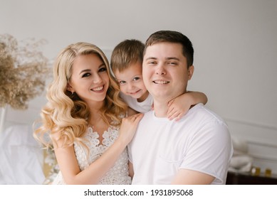 Beautiful young family man woman and son in white clothes play on the bed at home