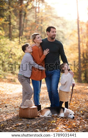 Beautiful young family with small children and dog standing in autumn forest.