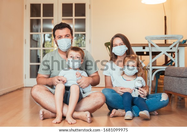 Beautiful young family wearing face\
masks against coronavirus world pandemic and staying\
home