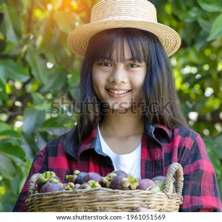 Beautiful young farmer holding basket of magoesteen fruit and smile in organic farm