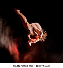 Beautiful young female athlete flying upside down outdoor at dark time. Red light and smoke around her - Powered by Shutterstock