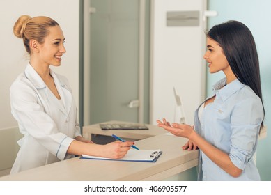 Beautiful Young Female Doctor Is Talking With Patient And Smiling, Standing In Waiting Room Of The Clinic