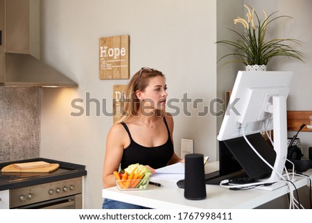 Beautiful young female freelancer working while sitting salad at table in apartment