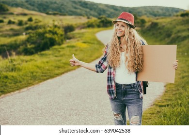 Beautiful young female holding blank cardboard and hitchhiking at the country road.Woman hitchhiking at the countryside
Image is intentionally toned. - Powered by Shutterstock