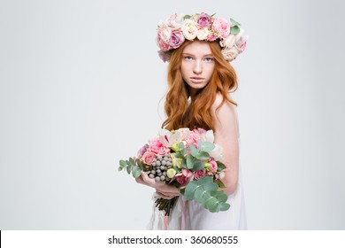 Beautiful young female with long red hair in wreath of roses posing with flower bouquet over white background – Ảnh có sẵn