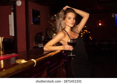 beautiful young female with makeup and hairstyle in a black dress with a glass of wine