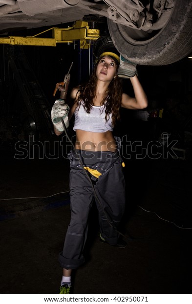 Beautiful young female mechanic inspecting car\
in auto repair shop. Girl welder is prepared to connect parts. Sexy\
mechanic