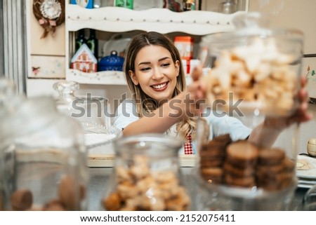 Beautiful young female seller working in a confectionery shop or bakery. She is selling and packing delicious sweets.