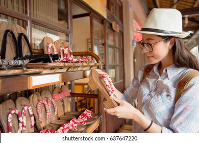 beautiful young female tourist in japan traditional street shopping and select japanese komageta shoes on cultural trip travel with family.