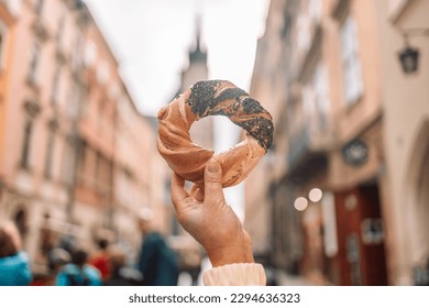 Beautiful young female tourist in stylish clothes holding pretzel obwarzanek on the market square in Krakow in Poland. High quality photo - Powered by Shutterstock