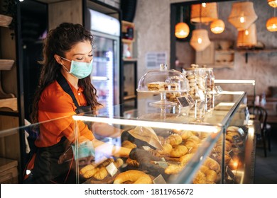 Beautiful young female worker with protective mask on face working in bakery. - Powered by Shutterstock