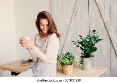 beautiful young feminine woman relaxing at home in lazy weekend morning with cup of coffee, wearing casual fashion clothes