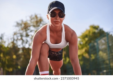 Beautiful young fitness girl is warming up at the stadium before training. Attractive slim brunette in a tracksuit, black cap and sunglasses. Active lifestyle. - Powered by Shutterstock