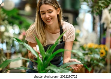 Beautiful young florist taking care of a plant while spraying it with water and working in a flower shop - Powered by Shutterstock