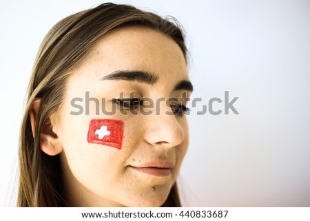 Beautiful young football fan woman with painted swiss flag on face closeup