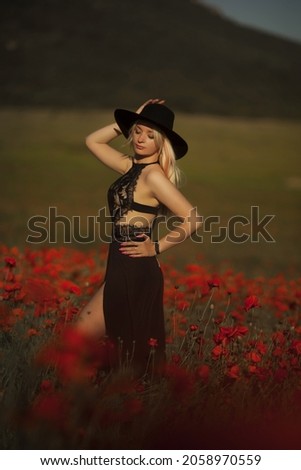 Beautiful young free girl in a hat in a summer field of red poppies with a bouquet. Soft selective focus