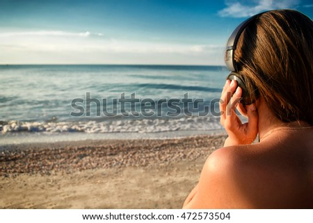 Beautiful young girl in bikini is listening music with headphones on the beach. With vignette