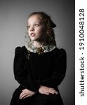 Beautiful young girl in black 1890s English Victorian 18th century child period dress with elegant white lace collar antique broach jewelery and long curly pretty hair looking away from camera