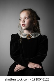 Beautiful young girl in black 1890s English Victorian 18th century child period dress with elegant white lace collar antique broach jewelery and long curly pretty hair looking away from camera