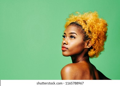 Beautiful young girl with bleached curly hair and bare shoulder looking up, in front of a green background