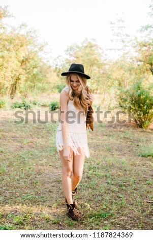 Beautiful young girl with blond hair in a suede jacket with fringed and black felt hat in the countryside on a sunny autumn day smiling
