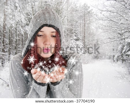 Beautiful young girl blowing snowflakes in white winter forest covered with snow