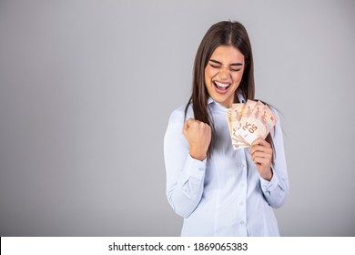 Beautiful Young Girl In A Blue Shirt With Euros In Hands On A Gray Background With A Surprised Face. Woman Holds Many Euro Bills Out Of Cash Prize, Lottery, Money Gift Or Inheritance