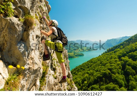 Beautiful young girl climbing Drachenwand via ferrata high above scenic Mondsee lake, Austria