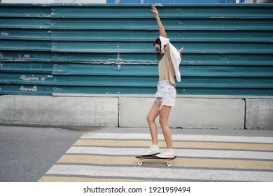 Beautiful young girl in denim shorts and snikers riding on the skateboard on the road in summer day. Side view. - Powered by Shutterstock