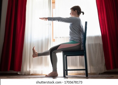 Beautiful young girl doing exercises at home sitting on chair