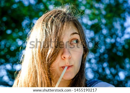 Beautiful young girl drinking a drink from a tube. He looks away in surprise. Bokeh in the background, summer.