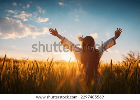 Beautiful young girl with flower chaplet, ethnic folklore dress with traditional Bulgarian embroidery during sunset on a wheat agricultural field