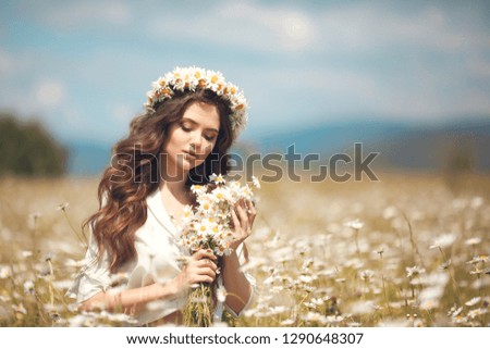 Beautiful young girl with flowers enjoying in chamomile field. Carefree happy brunette woman with chaplet on healthy wavy hair having fun outdoor in nature. People freedom style.