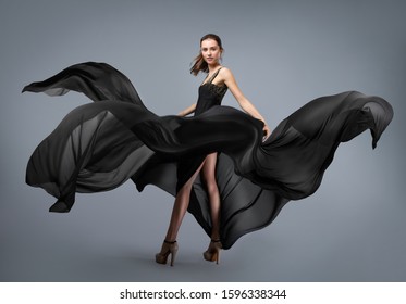 Beautiful Young Girl In Flying Black Dress. Flowing Fabric. Light Black Fabric Flying In The Wind