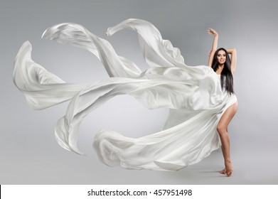 Beautiful Young Girl In Flying White Dress. Flowing Fabric. Light White Cloth Flying In The Wind