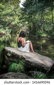 Beautiful young girl at forest, reading a book in a relax landscape nature river