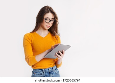 A Beautiful Young Girl In Glasses With A Tablet In Her Hands Poses On A Light Background. Education, Distance Learning. Space For Text