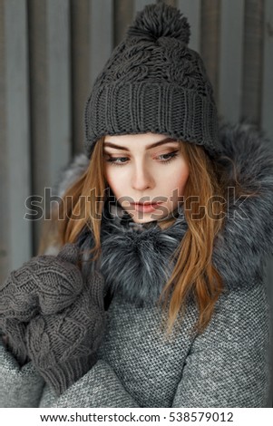 Beautiful young girl in a gray knitted hat and a mittens near the wooden wall