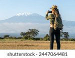 beautiful young girl In a hat stands against the backdrop of the Kilimanjaro volcano and looks away. The concept of tourism and African safari. female backpacker takes pictures of nature and animals