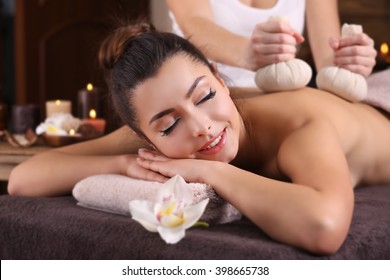 Beautiful young girl having massage with herbal balls in spa salon