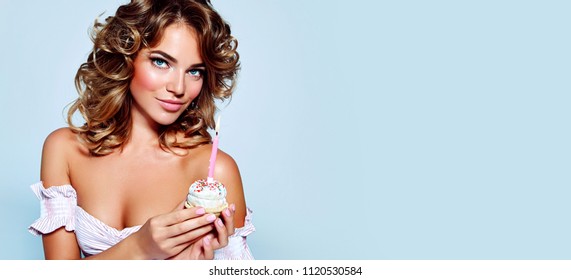 Beautiful young girl in her birthday with a lush hairdo in a pink dress in the style of pin holding a cake with a lighted candle. Birthday.