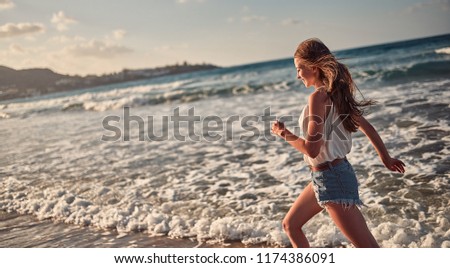 Beautiful young girl with her hair down running on the beach. Sea waves and clear sky in the background.