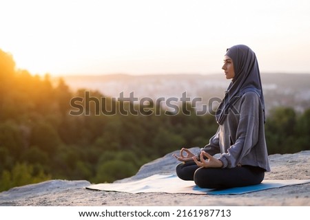 Beautiful young girl in a hijab meditates and practices yoga on a background of sunset and landscape. The concept of a healthy lifestyle