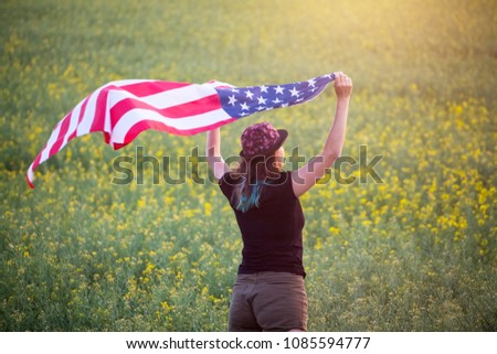 Beautiful young girl holding an American flag in the wind in the sunset. Celebrating 4th July concept