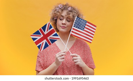 Beautiful young girl holding flags of USA and UK in her hands. Girl isolated in yellow background studio. Dressed in pink shirt and wearing flowers in her hair. Concept of English Speaking countries.  - Powered by Shutterstock